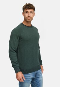 Mørkegrøn strikket sweater med ribstrikket kant og manchetter, design med rund hals, parret med lyseblå denim jeans. Glat tekstur, medium tykkelse.