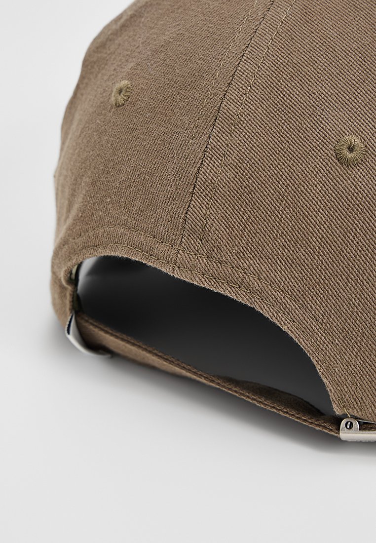 Gorra de béisbol marrón hecha de tela texturizada, con un ala curva, ojales cosidos y una correa ajustable de metal plateado en la parte posterior.