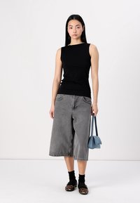 Black sleeveless top, gray wide-leg denim culottes, black socks, and leopard print shoes. Holding a small blue handbag. Simple background.