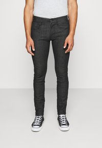 Jeans de mezclilla oscuros de corte ajustado con una textura suave, que cuentan con bolsillos frontales y cierre de botón, combinados con zapatillas negras.