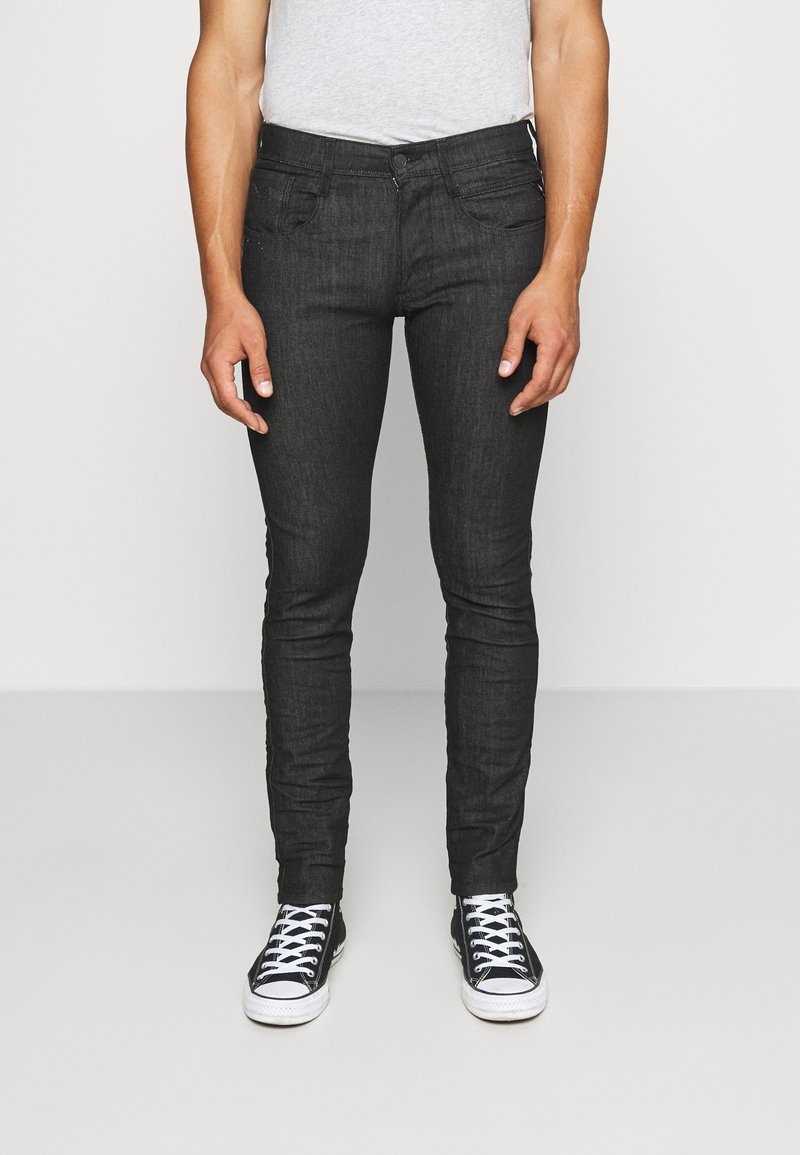 Jeans de mezclilla oscuros de corte ajustado con una textura suave, que cuentan con bolsillos frontales y cierre de botón, combinados con zapatillas negras.