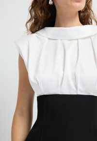 Jurk met een witte, geplooide, semi-doorzichtige top met een opgerolde kraag en een aansluitende zwarte rok. Vlotte stof, elegante silhouet.