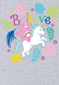 Unicornio blanco con melena azul y cuerno dorado lleva un oso rosa con barriguita de arcoíris. Rodeado de un follaje colorido y la palabra "Cree".