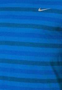 Sininen Nike-t-paita, jossa on vaaleansinisistä ja tummansinisistä vaakasuoria raitoja. Paita on valmistettu teksturoidusta kankaasta ja siinä on pieni hopeinen logo kauluksen lähellä.