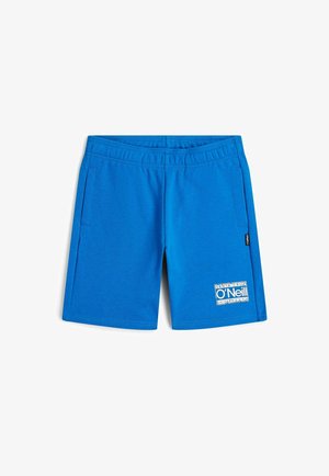 Červená mikina s kapucňou, predným vreckom a bielym logom. Kombinovaná s modrými kraťasmi s malou nášivkou loga. Nosená s čiernymi žabkami.