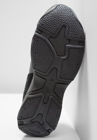 Mustan urheilu kengän pohja, jossa on teksturoitu pinta, erilaisia kulutuspintoja ja korostettu, kohotettu keskiosa pitoa varten.