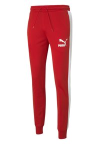 Red athletic pants with white side stripes, elastic waistband with drawstring, and a white Puma logo on the left hip. Smooth fabric texture.
