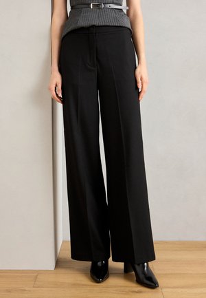 Black, wide-leg trousers with a smooth texture, high waist, and sharp crease line; paired with black pointed-toe heels.
