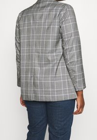 Grå rutig kavaj med en strukturerad design, med slagkrage och långa ärmar. Materialet är texturerat med vita och svarta mönster.