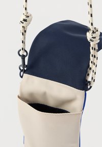 Granatowo-beżowy materiałowy woreczek o fakturowanej powierzchni, wyposażony w przednią kieszeń oraz pleciony pasek z detalem w postaci supełka.