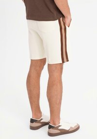 Krämfärgade shorts med bruna vertikala ränder på varje sida, fickor och en avslappnad passform. Matchat med lågt profilskor i neutrala färger.