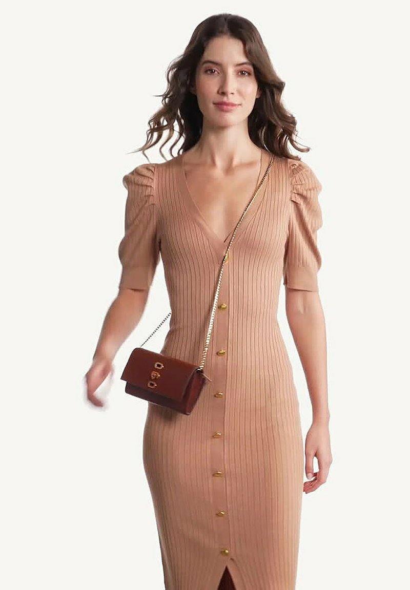Robe beige à rayures avec de courtes manches bouffantes, un décolleté en V profond et des accents de boutons dorés. Associée à un petit sac à main marron avec une bandoulière en chaîne.