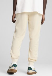 Beige sweatpants med smal ben, forsynet med manchetter ved anklerne, og en blød tekstur, kombineret med lave hvide sneakers med grønne og lilla detaljer.