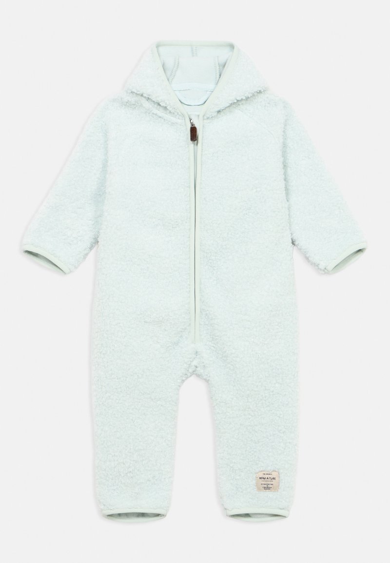 Grenouillère en polaire bleu clair avec fermeture éclair, capuche et poignets côtelés. Présente un tissu doux et texturé ainsi qu'une petite étiquette de marque sur la jambe.