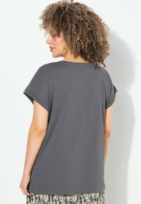Camiseta gris de manga corta con un corte relajado y mangas enrolladas, hecha de una tela suave. La parte de atrás presenta un ligero escote en forma de U.