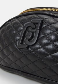 Musta tikattu nahkalaukku kultaisella vetoketjulla. Ominaisuuksiin kuuluu pokaallinen musta logo ja teksturoitu pinta, jossa on timanttimainen kuvio.