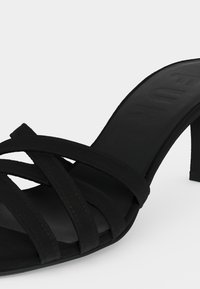 Μαύρο πέδιλο με ψηλό τακούνι και πολλαπλά λεπτά λουράκια που διασταυρώνονται πάνω από τα δάχτυλα και ανοιχτή μύτη.