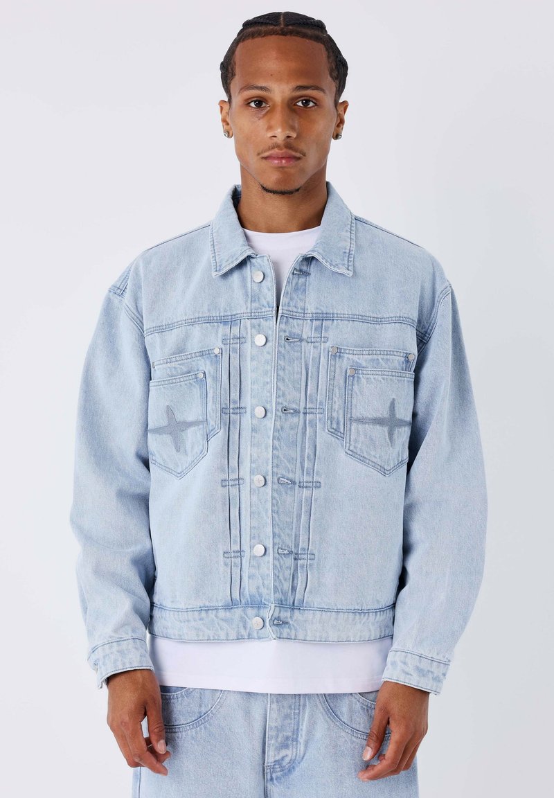 Giacca in denim azzurro chiaro con taglio classico, caratterizzata da due tasche frontali, chiusure con bottoni e dettagli di cuciture sottili sul petto.