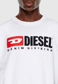 Hvid bomulds T-shirt med "DIESEL" logoet i fed sort og rød broderi, med "DENIM DIVISION" trykt nedenunder i mindre tekst.