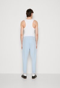 Light blue joggers with elastic waistband and ribbed cuffs, paired with a white tank top, viewed from the back. Smooth fabric texture.