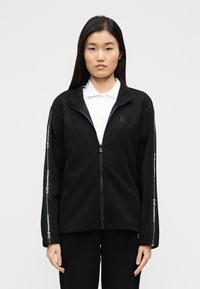 Zwarte sweatjas met rits en hoge kraag, met een gladde textuur, logodetail op de borst en bedrukte tekst langs de mouwen.