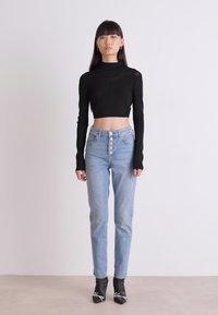 Svart långärmad crop top, högmidjade ljusblå jeans med femknäppning, och svarta spetsiga stövlar. Enkelt mönster och åtsittande siluett.