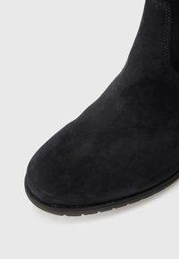 Black suede ankle boot toe with a rounded shape and visible stitching near the top edge and sole.