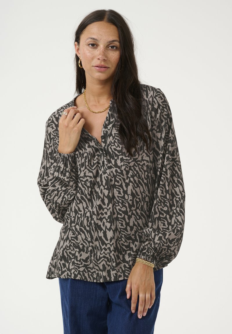 Blouse à manches longues en gris foncé avec un motif abstrait clair. Caractéristiques d'un décolleté boutonné et de manches élastiques. Portée avec un jean bleu.