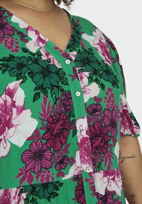 Grünes Blumenmusterkleid mit pinken und dunkelgrünen Blumen. Besitzt einen V-Ausschnitt, kurze Ärmel und weiße Knöpfe auf der Vorderseite. Weicher Stoff.