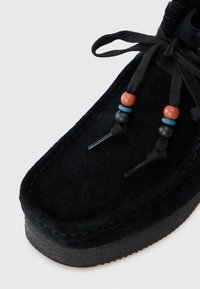 Scarpa in suede nera con forma arrotondata, dotata di lacci testurizzati e perline decorative multicolori. Sole in gomma nera, cuciture visibili.