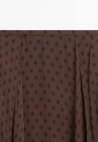 Brown fabric with black polka dots, featuring a textured surface and vertical pleats, creating a layered appearance.