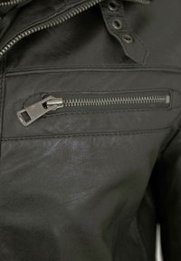 Schwarze Lederjacke mit einer mit einem Metallreißverschluss versehenen Brusttasche und strukturiertem Material, das ein elegantes Design präsentiert.