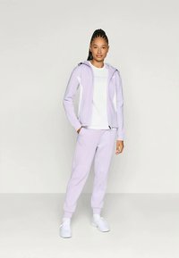 Vaaleanlila vetoketjuhuppari, jossa on samat sävyiset joustavat housut; hupussa valkoiset yksityiskohdat; sileä rakenne; käytetty valkoisten lenkkareiden kanssa.