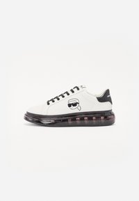 White sneakers with a black heel accent, featuring a cartoon logo on the side, and a thick translucent sole with a black and purple gradient.