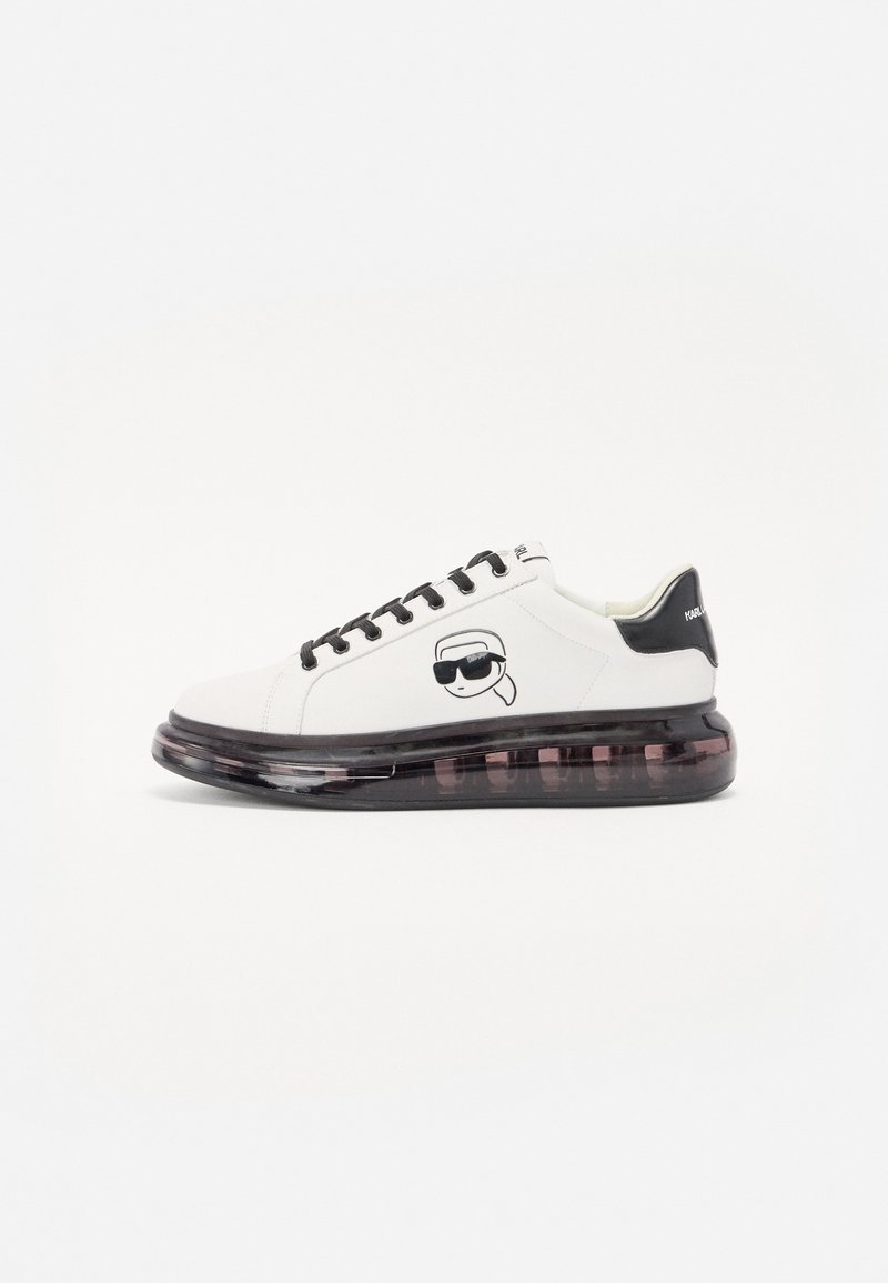 White sneakers with a black heel accent, featuring a cartoon logo on the side, and a thick translucent sole with a black and purple gradient.
