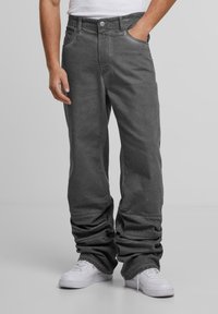 Harmaat löysät puuvillapantsit, joissa on sileä rakenne, viisi taskua ja nappisuljenta. Yhdistetty valkoisiin lenkkareihin.