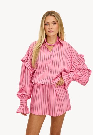 Camisa de rayas rosas con mangas con volantes y pantalones cortos a juego. La tela es ligera, con rayas verticales en diferentes tonos de rosa.