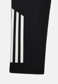 Svarta atletiska leggings med tre vertikala vita ränder på vänster sida; slät textur med en åtsittande design och fållad nederkant.