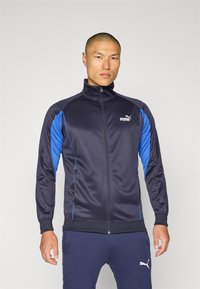 Mørkeblå zip-up treningsjakke laget av glatt polyester, med blå detaljer og Puma-logoen på brystet, samt ribbestrikkede mansjetter.