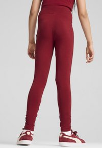 Burgundy leggings med hög midja, med en slät textur och åtsittande silhuett; matchande burgundy sneakers med krämfärgade accenter.