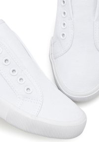 Weiße Sneakers aus Canvas mit niedrigem Schnitt, ausgestattet mit sechs Ösen, strukturiertem Stich und einer Gummisohle mit gerippten Details.
