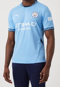 Vaaleansininen jalkapallopaita hengittävästä materiaalista, jossa pyöreä kaula-aukko, kontrastikuvioidut hihansuut ja valkoiset logot: Etihad Airways ja Manchester City.