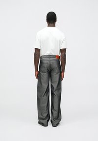 Pelēki plataji džinsa svārki ar teksturētu virsmu, aizmugurē pie vidukļa ar brūnu ādas etiķeti un vienkāršu balto T-kreklu.