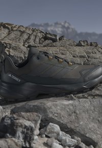 Chaussure de randonnée Adidas Terrex noire sur un terrain rocheux avec un paysage montagneux flou en arrière-plan.