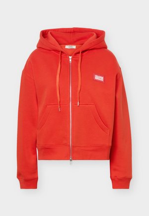 Piros cipzáras kapucnis pulóver elülső zsebekkel, húzózsinóros kapucnival és kis téglalap alakú logó címkével a bal mellrészen.