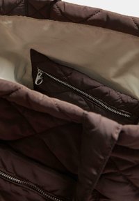 Borsa a mano marrone trapuntata con un interno liscio, dotata di una tasca con zip e dettagli in metallo argentato. L'esterno presenta un motivo testurizzato.