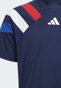 Camiseta deportiva de color azul marino con franjas diagonales en rojo, blanco y azul en los hombros. Presenta un cuello redondo y un logotipo impreso en blanco.