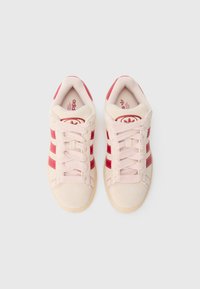 Rozā zamšādas kedas ar sarkaniem svītrām, apaļu purngalu, auklu stiprinājumu priekšpusē un polsterētu iekšpusi. Plakana gumijas zole. Ikoniskais logotips uz mēlītes.