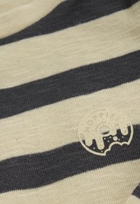 Close-up van zwart en crèmekleurig horizontaal gestreept stof met een klein donutvormig logo waarop het woord "NORFIKS" staat.