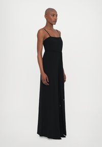 Black, floor-length dress with thin straps, a squared neckline, and a sleek silhouette. Fabric appears smooth with a slight sheen.